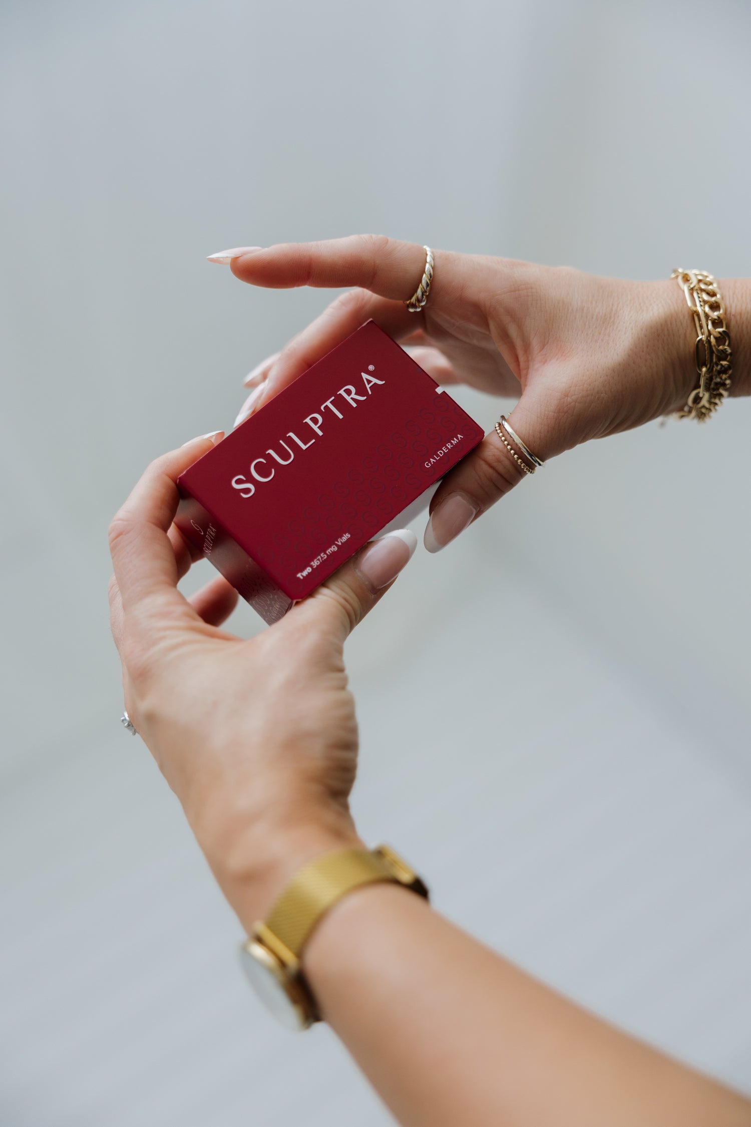 A person holding a red Sculptra box with gold jewelry