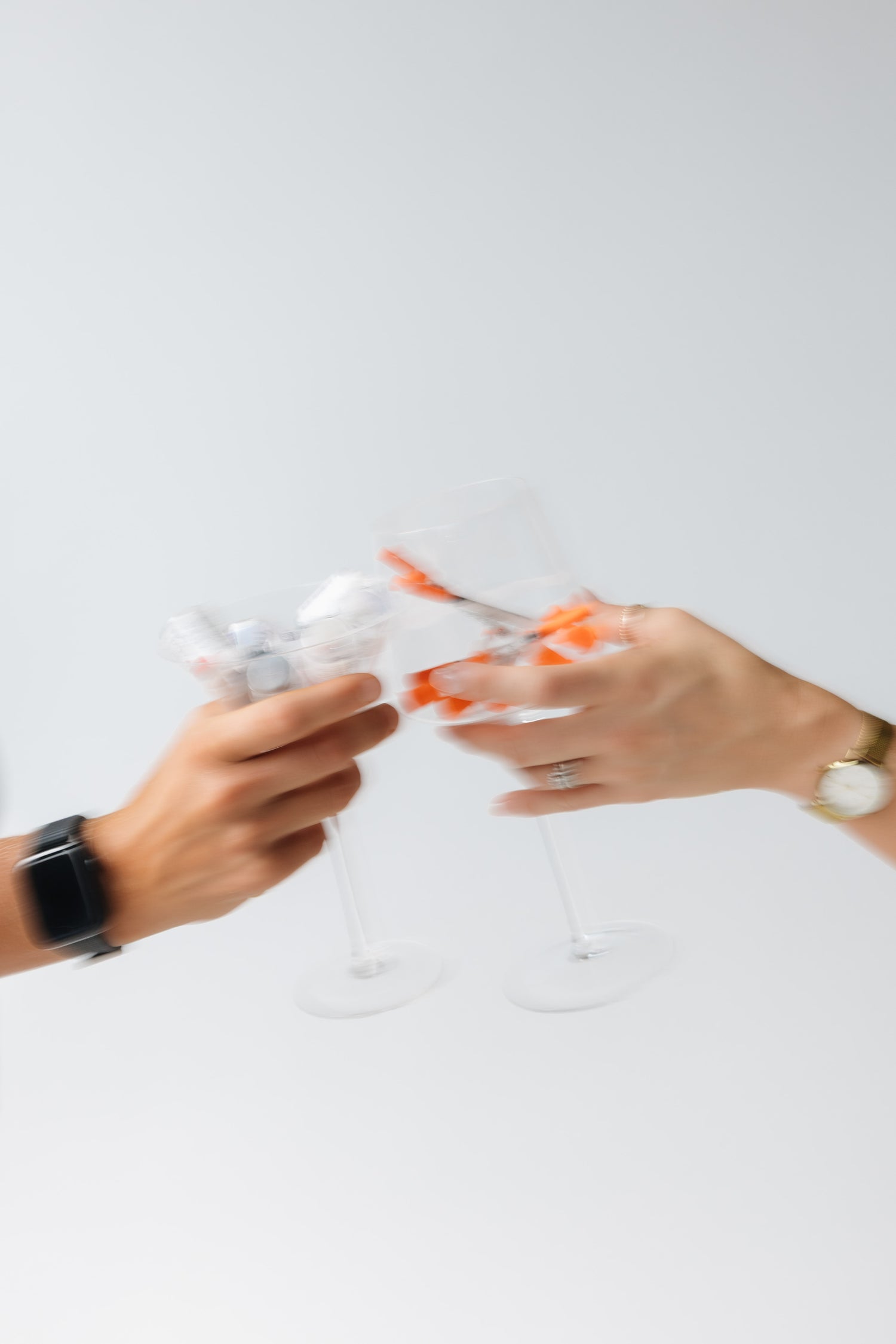 Two hands clinking cocktail glasses together in a blurred toast.
